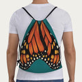 Model wearing jade‑green drawstring backpack showing full‑scale monarch butterfly wings printed across the back panel.