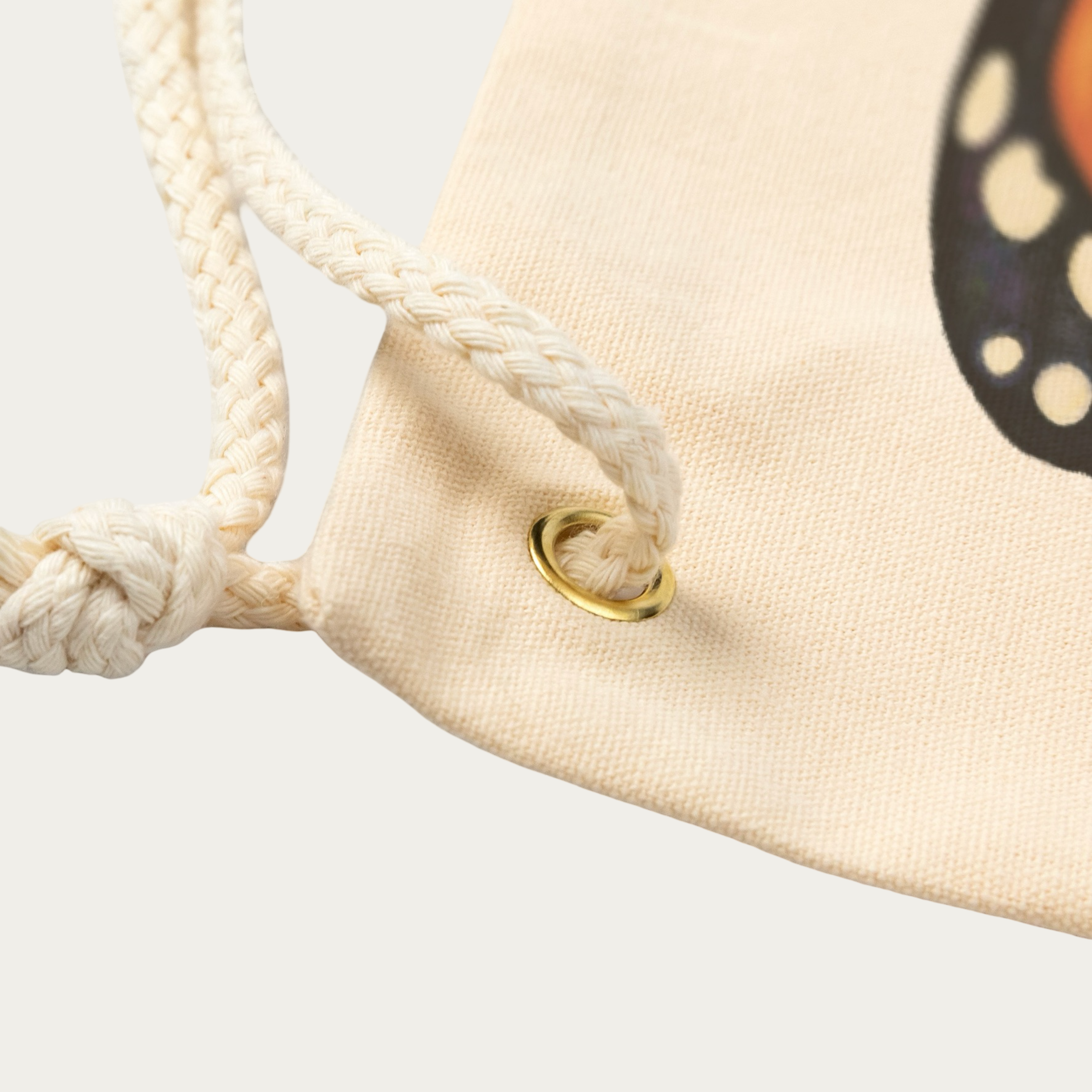 Close‑up of natural‑canvas drawstring backpack corner showing rope drawstring, metal grommet, and canvas weave.