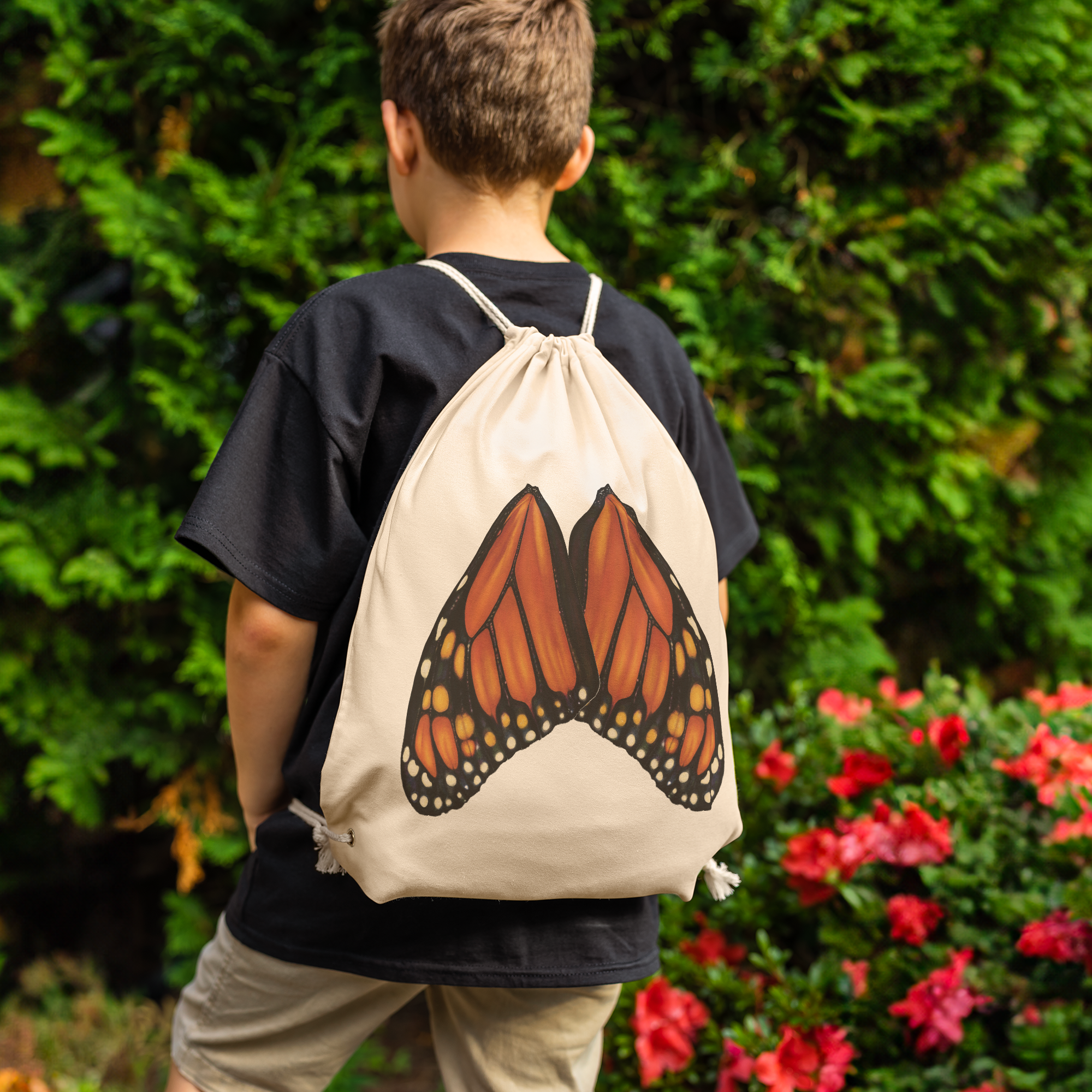 Model wearing natural‑canvas drawstring backpack showing full‑scale monarch butterfly wings printed across the back panel.