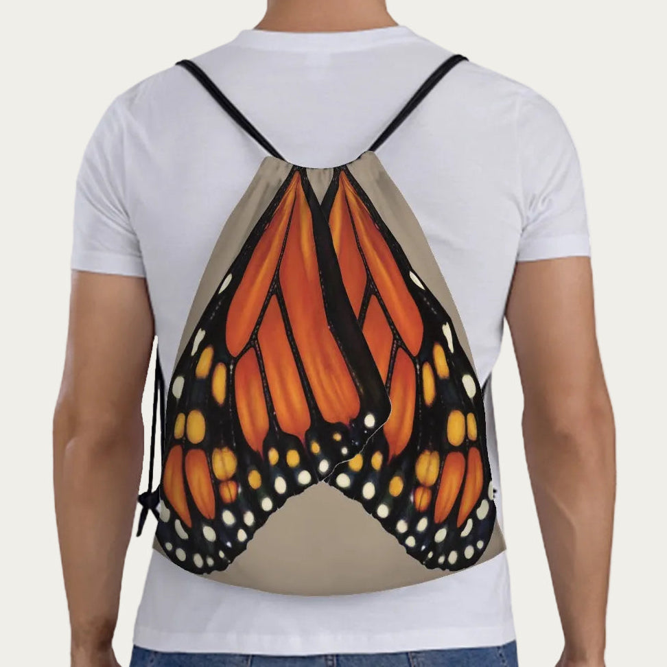 Model wearing sand drawstring backpack showing full‑scale monarch butterfly wings printed across the back panel.