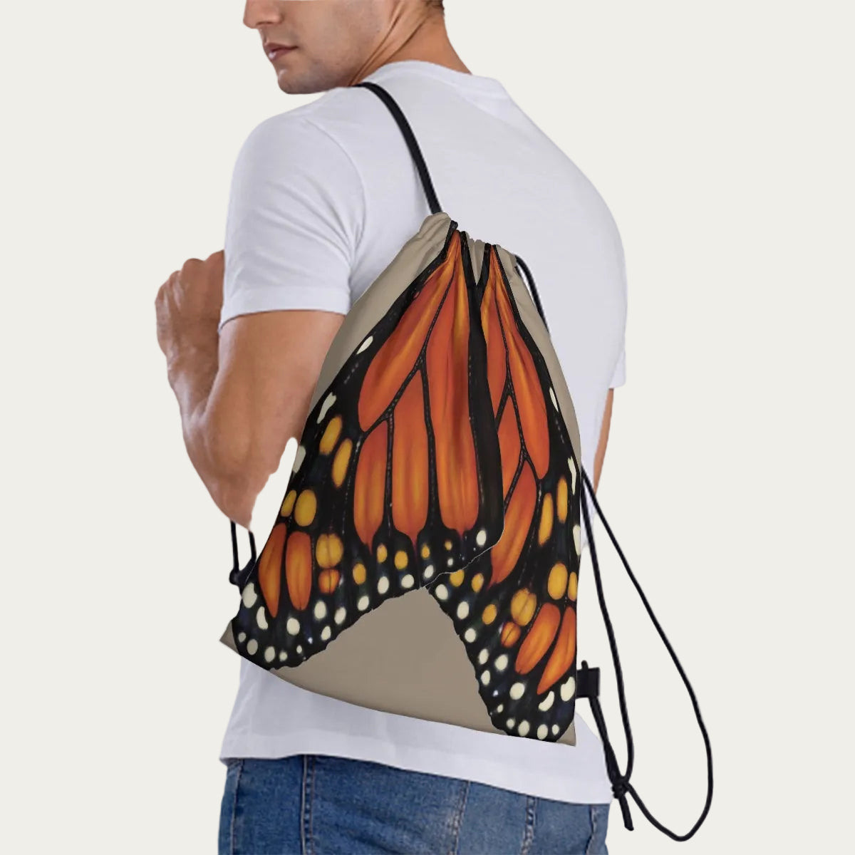 Model wearing sand drawstring backpack slung over one shoulder, showing side view of the monarch wing artwork.