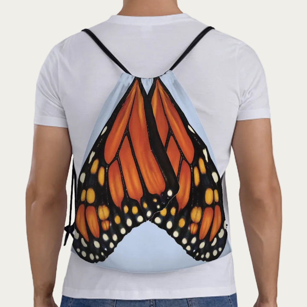 Model wearing sky‑blue drawstring backpack showing full‑scale monarch butterfly wings printed across the back.