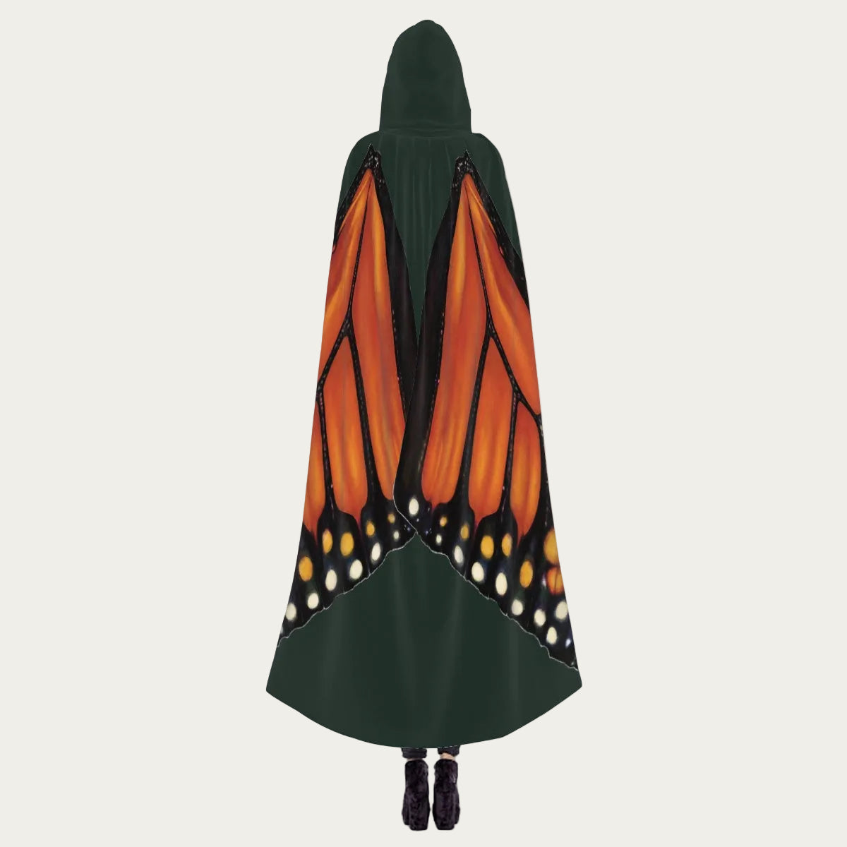 Model standing with back facing camera wearing hunter green hooded cape showing monarch butterfly wings draping naturally down the back.