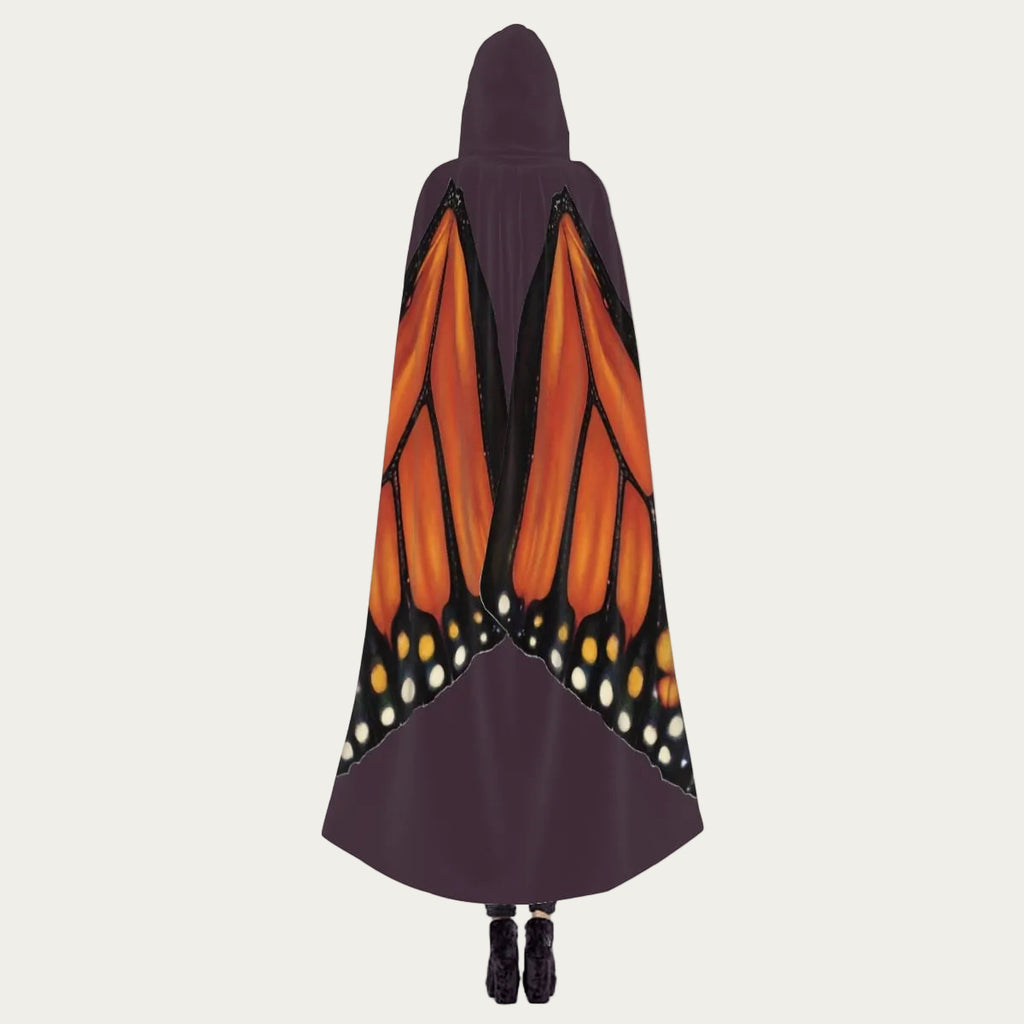 Model standing with back facing camera wearing plum hooded cape showing monarch butterfly wings draping naturally down the back.