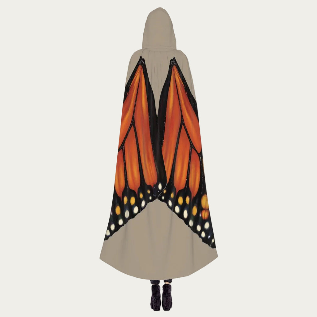 Model standing with back facing camera wearing sand hooded cape showing monarch butterfly wings draping naturally down the back.