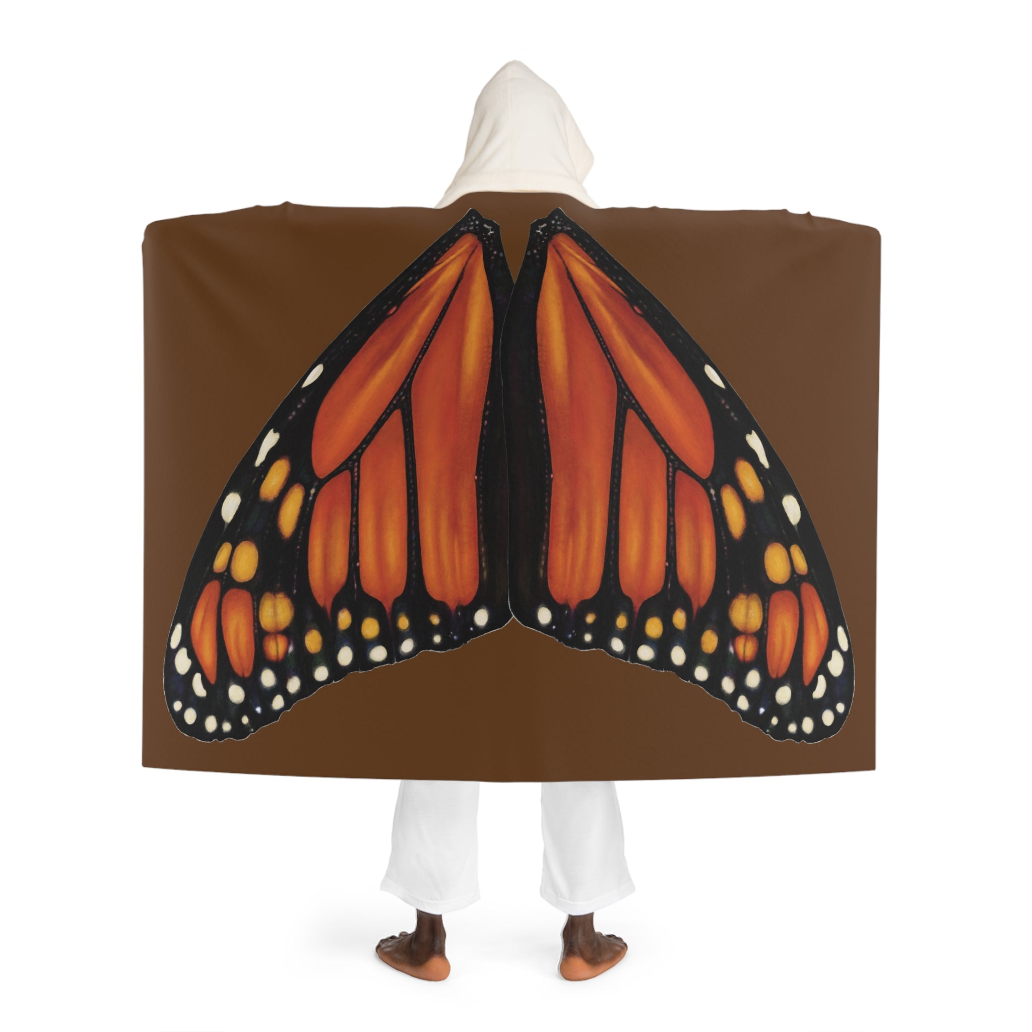 Model standing with back facing camera wearing brown hooded sherpa blanket showing monarch butterfly wings printed across the back and cream sherpa‑lined hood.
