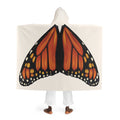 Model standing with back facing camera wearing cream hooded sherpa blanket showing monarch butterfly wings printed naturally across the back and cream sherpa‑lined hood.