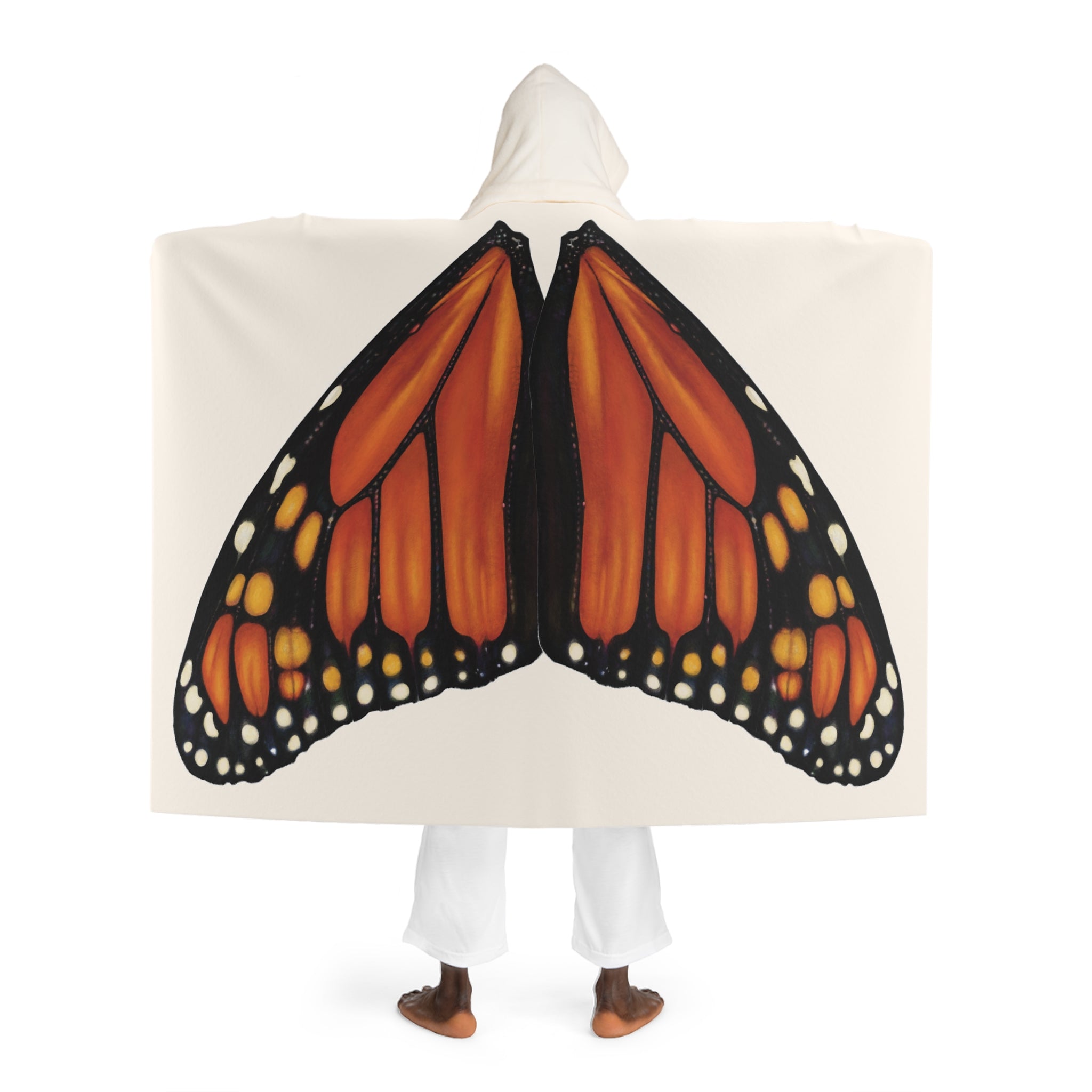 Model standing with back facing camera wearing cream hooded sherpa blanket showing monarch butterfly wings printed naturally across the back and cream sherpa‑lined hood.