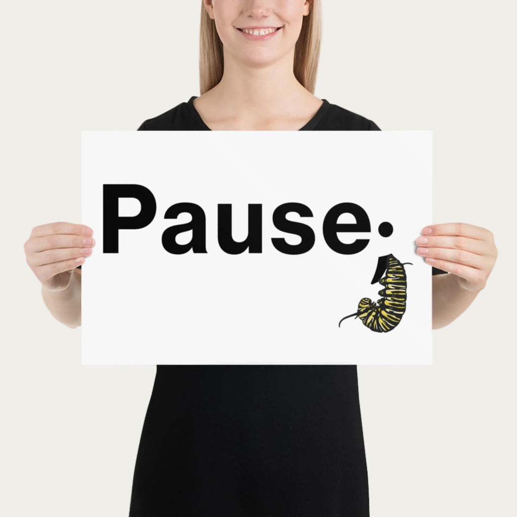 Model holding 12×18 art print at chest height displaying the minimal “Pause.” design with monarch caterpillar illustration centered on matte paper.