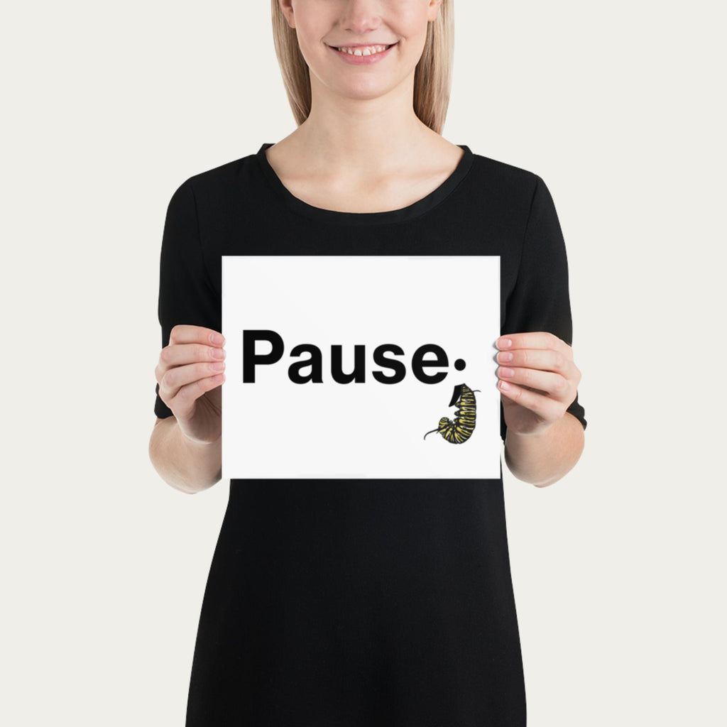 Model holding 8×10 art print at chest height showing the word “Pause.” with a monarch caterpillar curled into its natural resting posture.