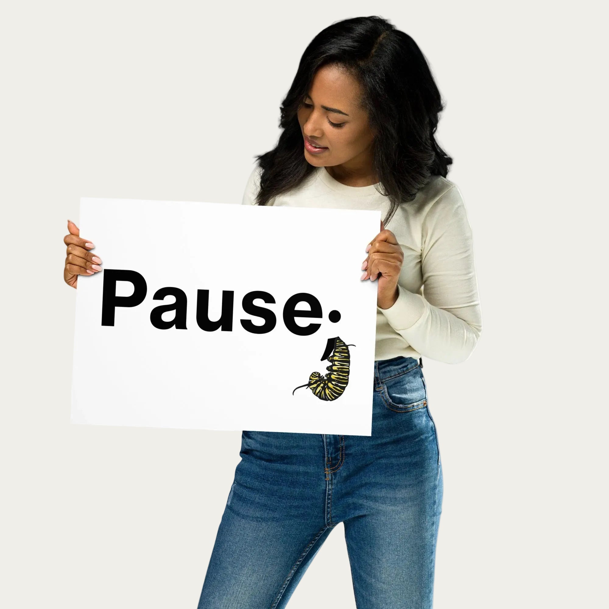 Model holding art print while turned slightly to the side, showing the “Pause.” text and monarch caterpillar illustration on matte paper.