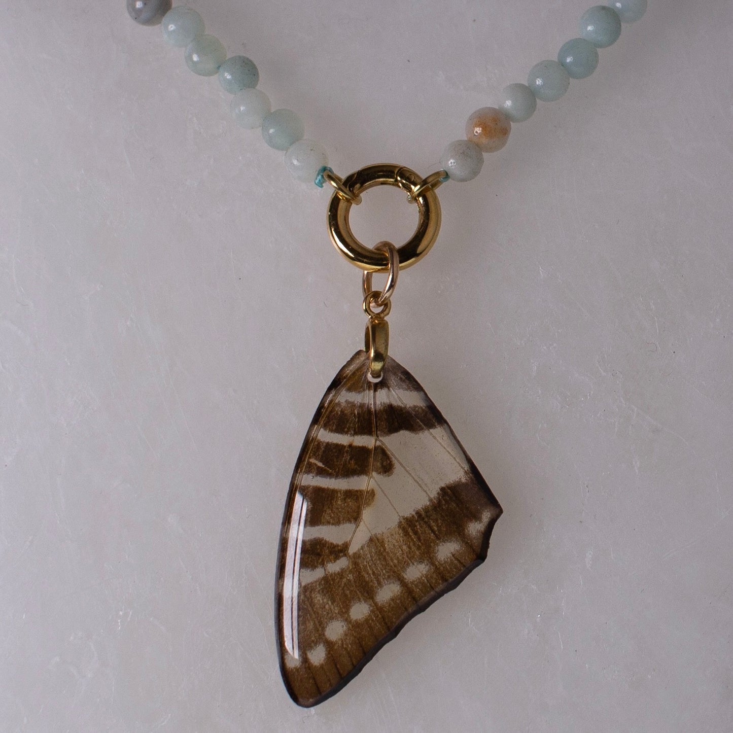 real butterfly wing necklace blue stone beaded gold metalwork close up on wax