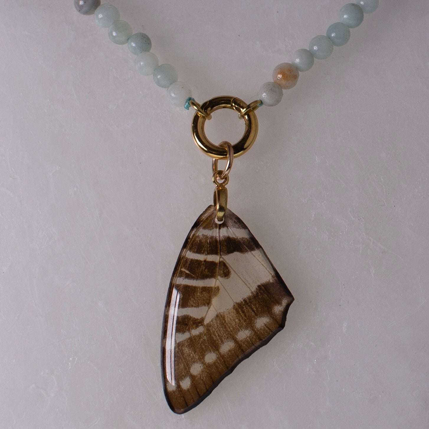 real butterfly wing necklace blue stone beaded gold metalwork close up on wax