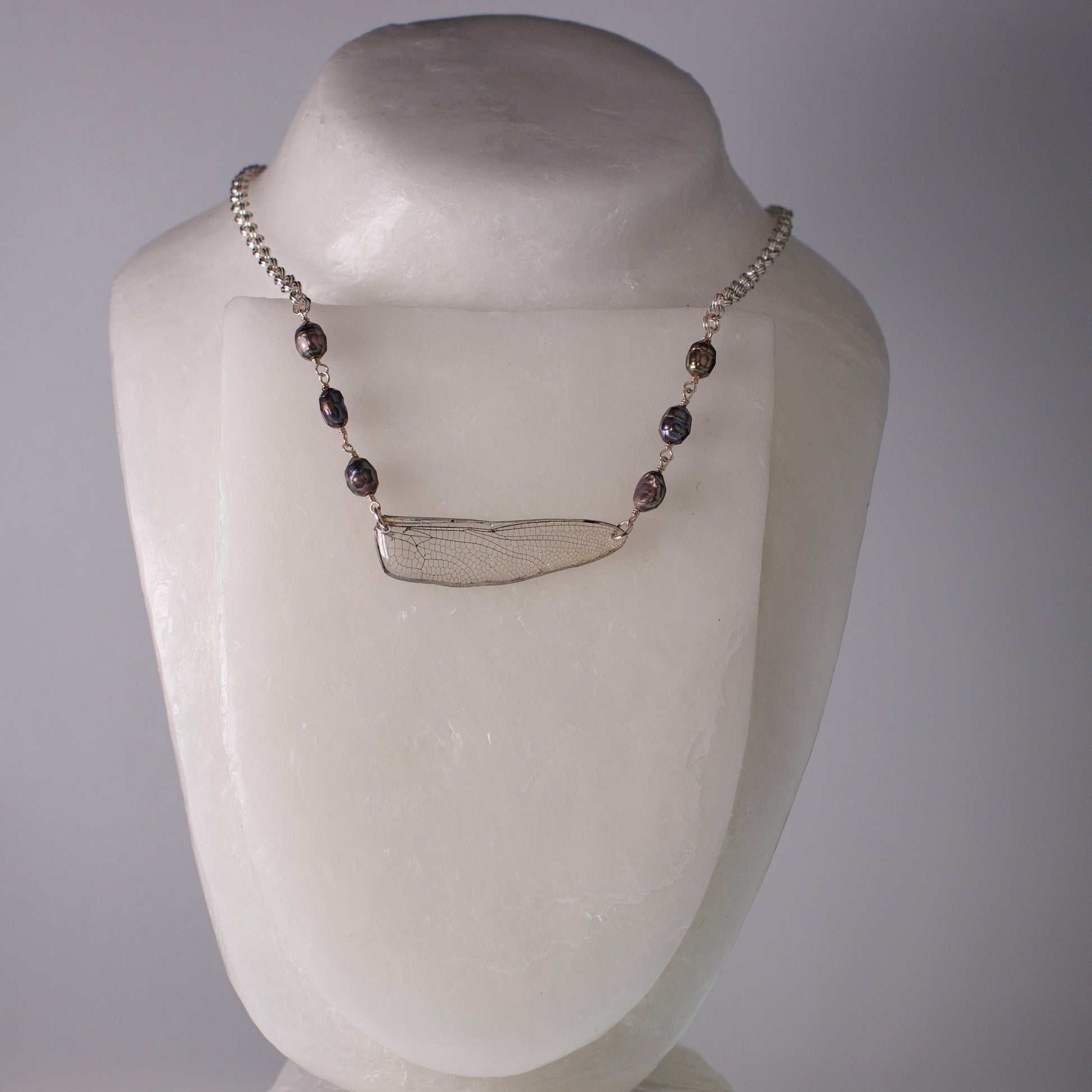 real dragonfly wing necklace iridescent pearls silver chain on wax from grey background